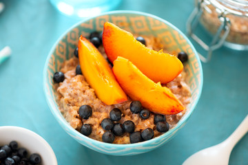 Porridge bowl oatmeal with peach and blueberries on turquoise backgraund. Soft focus. Healthy eating concept. Top view