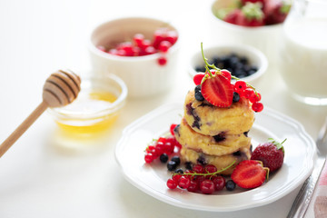 Stack of pancakes (syrniki) with strawberry, red currant and blueberries on white backgraund. Soft focus. Healthy eating concept