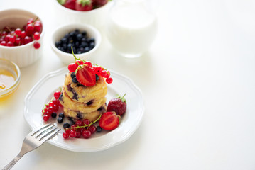 Stack of pancakes (syrniki) with strawberry, red currant and blueberries on white backgraund. Soft focus. Healthy eating concept
