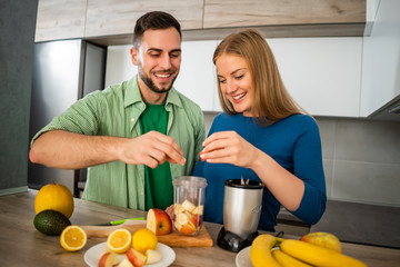 Young couple is preparing juice in their kitchen. 