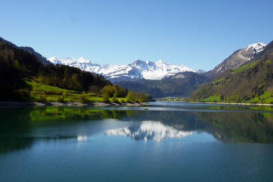 Lake Lungern in Switzerland with snow-capped mountain range reflecting in crystalline waters. © Rosmarie