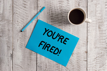 Conceptual hand writing showing You Re Fired. Concept meaning Used by boss indicate employee that he is discharged from job Pastel Colour paper and pen with coffee cup on wooden table