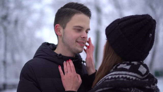 Young woman and tall man looking into each other's eyes in winter clothing. Woman caress face of boyfriend. Happy couple in love enjoy time together. Date of young couple.