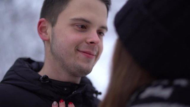 Young cute woman and tall man looking into each other's eyes in winter clothing. Woman caress face of boyfriend. Happy couple in love enjoy time together. Date of young couple.