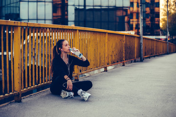 Female runner sitting on the bridge and drinking water from a bottle