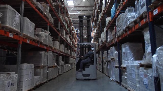 Camera movement between the racks with the goods. Ahead is a man on a forklift. 4K Slow Mo