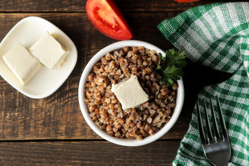Buckwheat. Porridge with a piece of butter in a glass plate on a brown wooden table. breakfast, healthy food. top view