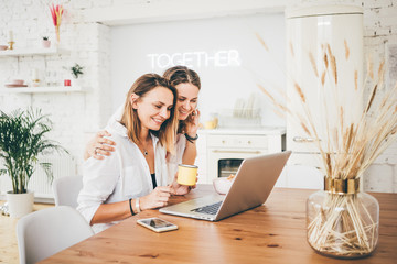 Two woman friends taking breakfast in the kitchen and having fun, talking and laughing.