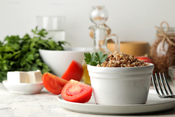 Buckwheat. Porridge cereals with parsley in a white ceramic bowl and tomato on a bright table. breakfast, healthy food.