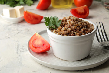 Buckwheat. Porridge cereals with parsley in a white ceramic bowl and tomato on a bright table. breakfast, healthy food.