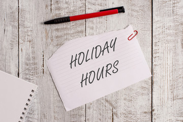 Word writing text Holiday Hours. Business photo showcasing employee receives twice their normal pay for all hours Torn paper and notebook sheet with a pen placed on top of wooden table