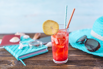Glass of red lemonade drink with lemon and fruit and straw on the table. Bright summer Sunny holiday in the resort.