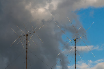 There are two metallic Amateur Radio ham antennas on the blue sky with gray and white clouds...