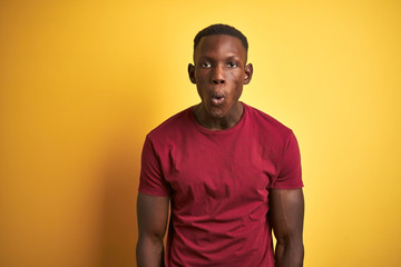 Young african american man wearing red t-shirt standing over isolated yellow background afraid and shocked with surprise expression, fear and excited face.