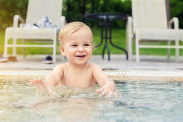 Happy little caucasian blond toddler boy swimming in wading pool on bright summer day at resort. Adorable baby enjoying outdoor water fun activities in shallow water. Children travel and holidays