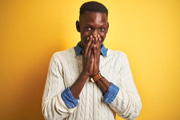 African american man wearing denim shirt and white sweater over isolated yellow background laughing and embarrassed giggle covering mouth with hands, gossip and scandal concept
