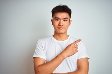 Young asian chinese man wearing t-shirt standing over isolated white background Pointing with hand finger to the side showing advertisement, serious and calm face