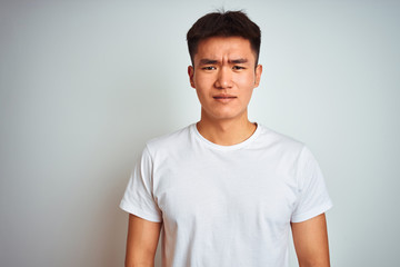 Young asian chinese man wearing t-shirt standing over isolated white background skeptic and nervous, frowning upset because of problem. Negative person.