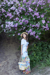 Beautiful girl enjoying the smell of lilac on a summer day. Aromatherapy and spring concept. A pretty girl, a beautiful woman in a blue long vintage dress is standing in a lilac garden. Gardening