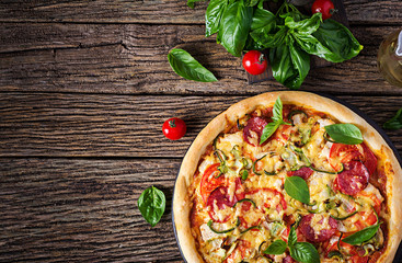 Italian pizza with chicken, salami, zucchini, tomatoes and herbs on vintage wooden background. Top view. Italian cuisine