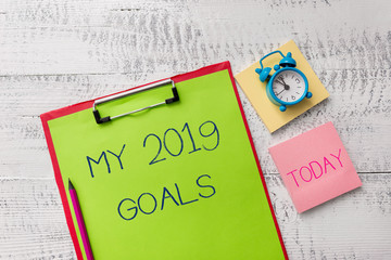 Handwriting text My 2019 Goals. Conceptual photo setting up demonstratingal goals or plans for the current year Metal clipboard sheets marker alarm clock notes pad wooden background