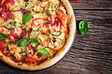 Italian pizza with chicken, salami, zucchini, tomatoes and herbs on vintage wooden background. Top view. Italian cuisine