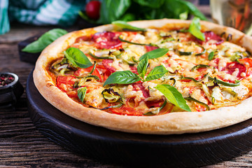 Italian pizza with chicken, salami, zucchini, tomatoes and herbs on vintage wooden background.  Italian cuisine