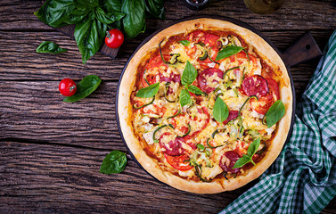 Italian pizza with chicken, salami, zucchini, tomatoes and herbs on vintage wooden background. Top view. Italian cuisine