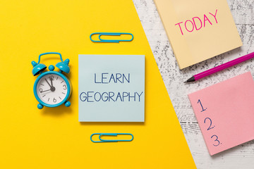 Handwriting text writing Learn Geography. Conceptual photo study of physical features of earth and its atmosphere Notepads clips colored paper sheet marker alarm clock wooden background