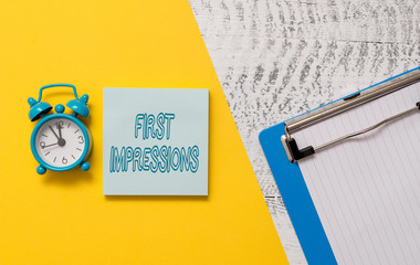 Conceptual hand writing showing First Impressions. Concept meaning What a demonstrating thinks of you when they first meet you Notepad colored paper sheet alarm clock wooden background