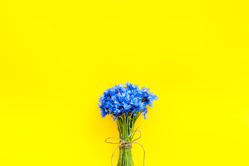 Field flowers design with bouquet of blue cornflowers on yellow background top view space for text