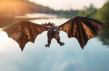 Naklejka premium terrifying powerful dragon, Handmade mystical creature with strong wings, reptile with spikes and long tail, evil serpent with devilish look attacks enemy, magical animal flies over lake at sunset