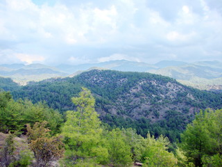 A panorama of the mountain ridge covered with thick green forest and sun-rustled rays against the background of heavy rain clouds on the horizon.