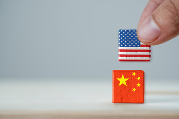 Fototapeta na wymiar Hand putting print screen USA flag on China flag wooden cubic with white background.It is symbol of tariff trade war tax barrier between United States of America and China.-Image.