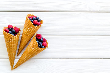 Fresh berries in waffle cones on white wooden background top view mock up