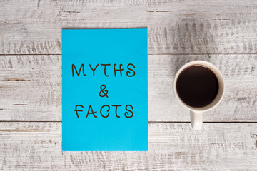 Conceptual hand writing showing Myths And Facts. Concept meaning usually traditional story of ostensibly historical events Stationary placed next to a coffee cup above wooden table