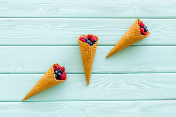 Fresh berries in waffle cones on mint green wooden background top view
