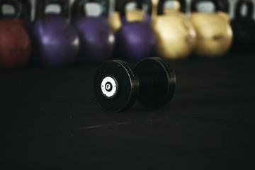 Gym equipment. The steel dumbbell stands  on the black rubber floor on the background of colorful weights.