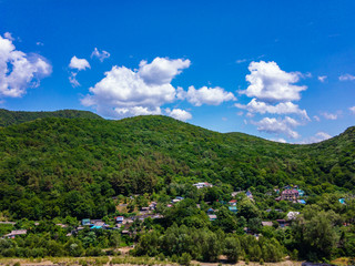 The village at the foot of the mountain, covered with green vegetation, against a blue sky with white clouds.