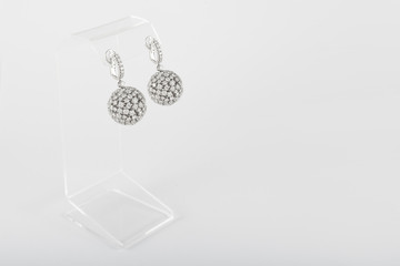 Fototapeta na wymiar Pair of white golden diamond earrings on transparent stand. Golden earrings with diamonds, luxury jewelry