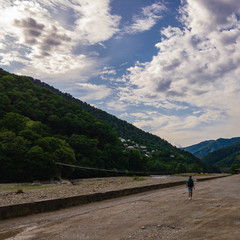 A man with a backpack is walking along the road towards the mountains on a summer day.