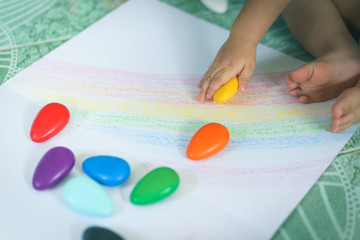 A hand of Asian baby boy drawing lines and shapes with colorful crayons.