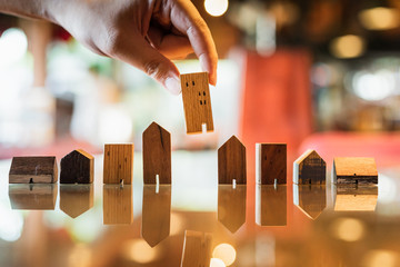Hand choosing mini wood house model from model and row of coin money on wood table, selective focus, Planning to buy property. Choose what's the best. A symbol for construction ,ecology, loan concepts
