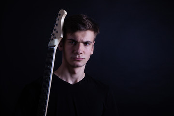Young caucasian adult posing with electric guitar in the studio. Black isolated background