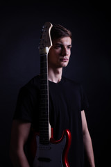 Young caucasian adult posing with electric guitar in the studio. Black isolated background