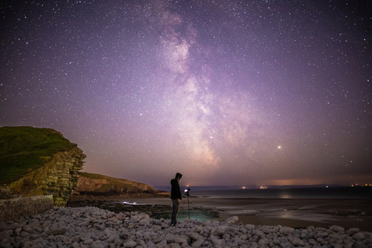 Stargazing photographer with camera and tripod on beach at night below Milky Way starscape