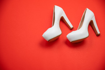White high heeled shoes, red background - top view concept - heels walking left