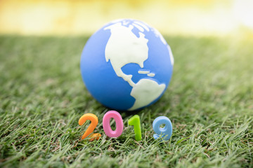 Fototapeta na wymiar Global new Year 2019 concept. Close up of colorful plastic toy number on grass with mini world ball.