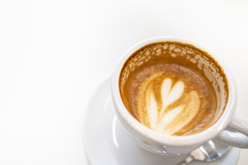 Close up of dirty white cup of hot coffee latte with heart shape art and white plate and spoon on with copy space for text.