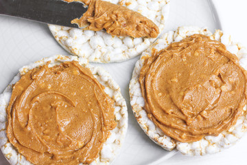 crunchy natural peanut butter sandwich with rice cake bread and knife with peanut butter on plate. Proper nutrition diet vegetarian breakfast
